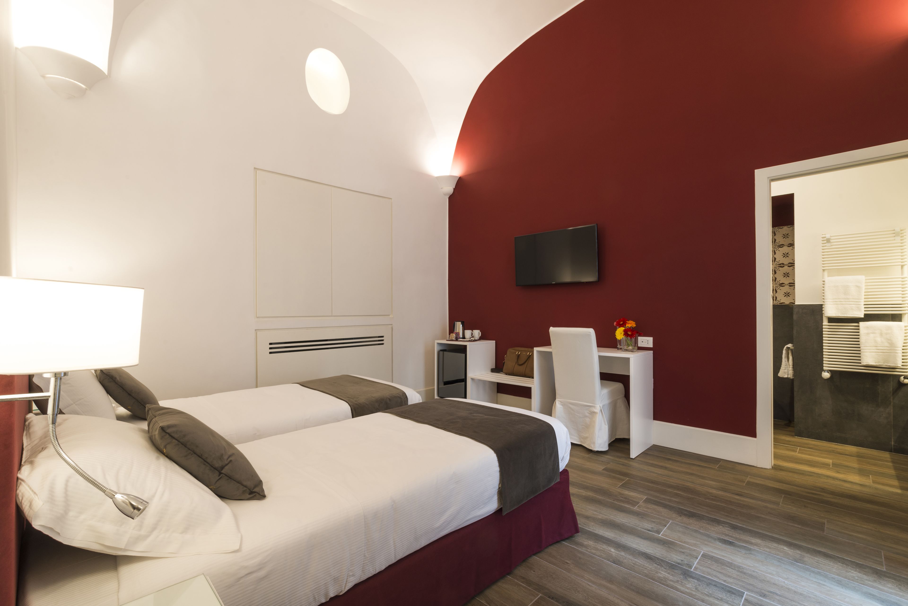 Une chambre d’hôtel avec deux lits, un bureau, une chaise, une télévision et une salle de bain visible à travers une porte ouverte.