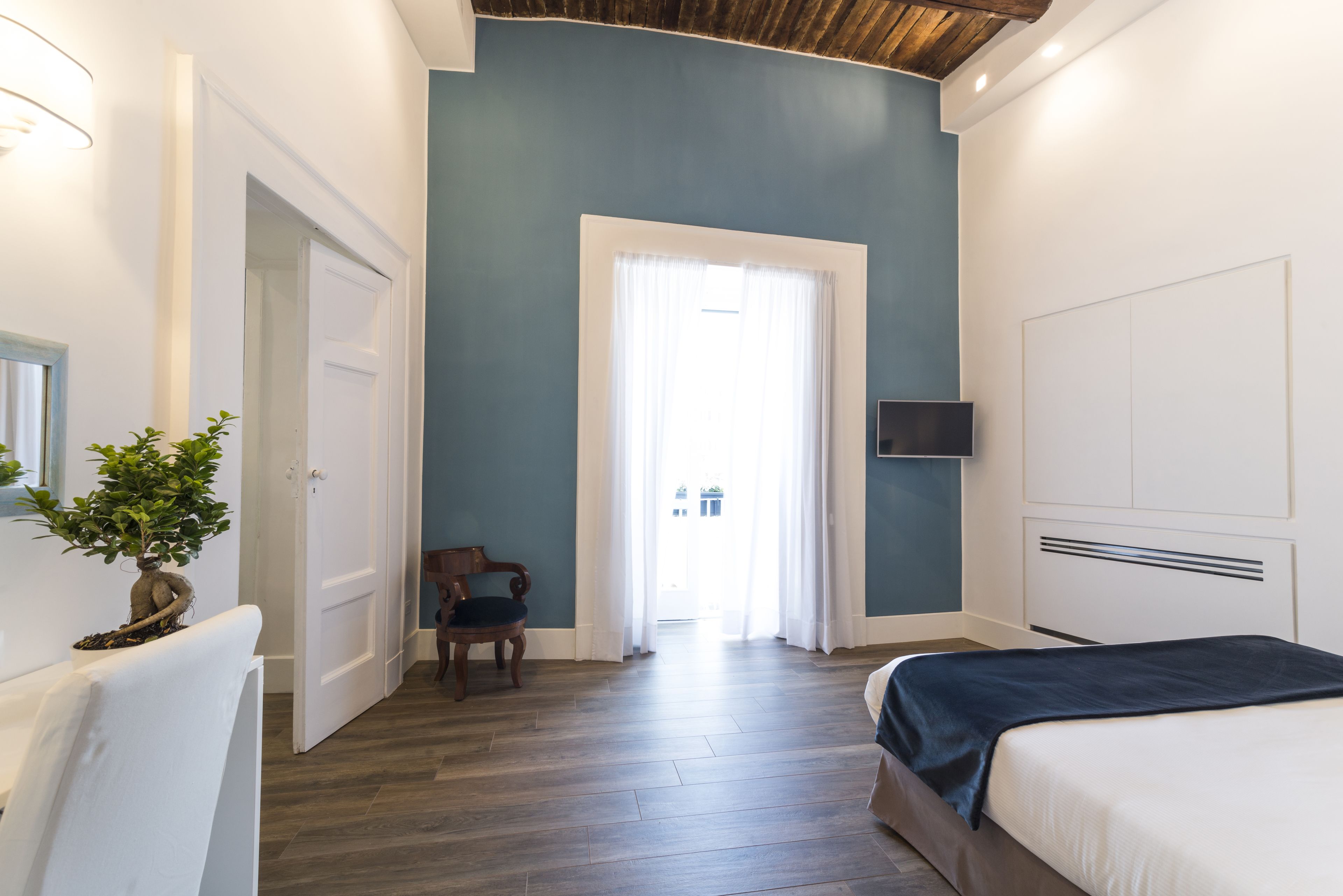 Une chambre à coucher comprenant un lit, une chaise, une plante en pot, un téléviseur et une porte donnant sur un balcon.