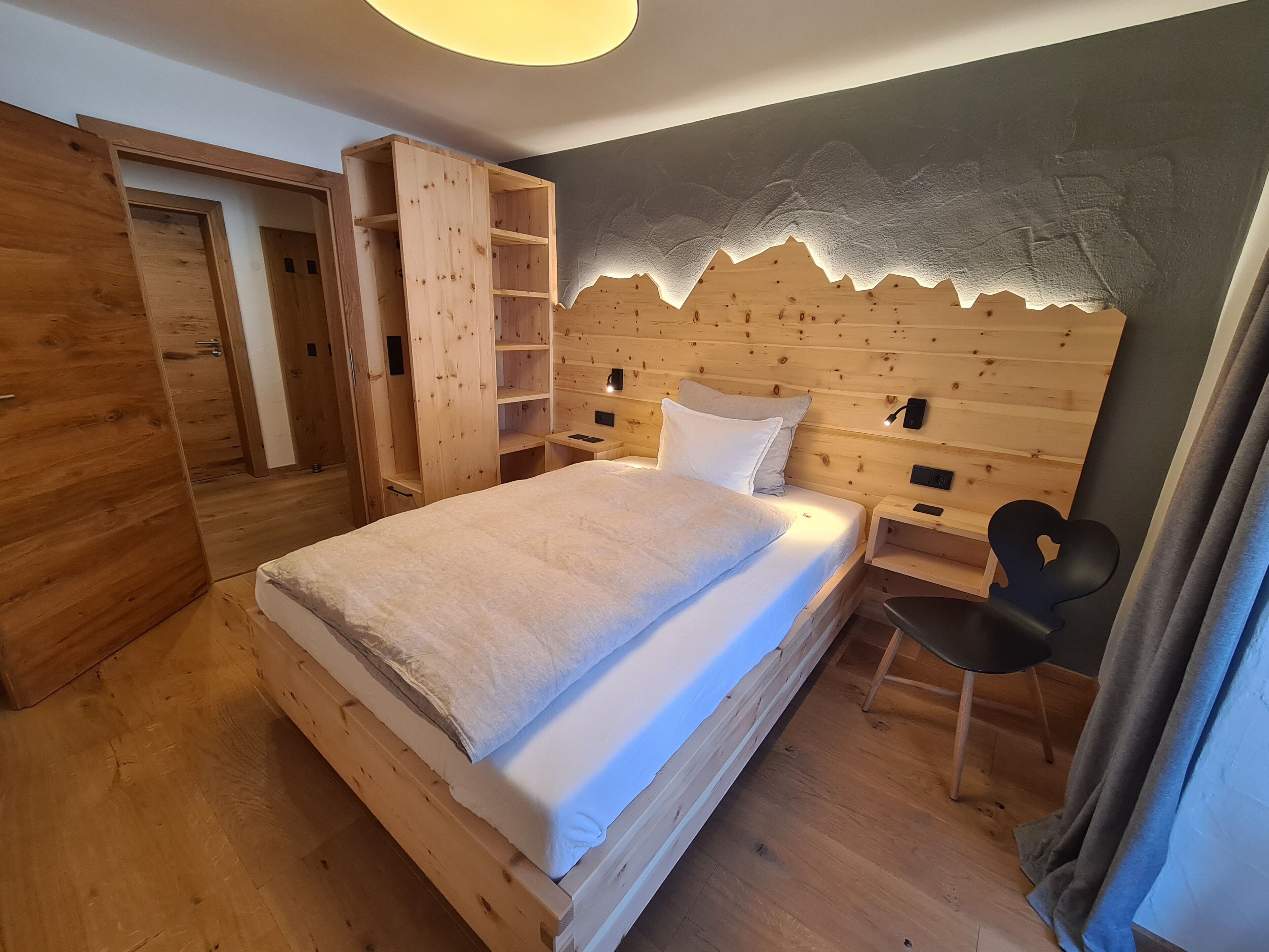 Un dormitorio de madera con cama, estanterías integradas y cabecera con diseño texturizado.