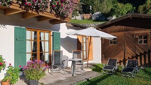 A chalet with a patio area featuring a table and chairs, a wooden deck, and potted plants. - AlpenNaturIdyll  (Grainau)