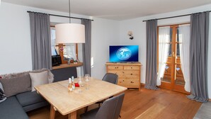 A modern living room with a wooden dining table, grey sofa, and a TV on a wooden cabinet. - AlpenNaturIdyll  (Grainau)