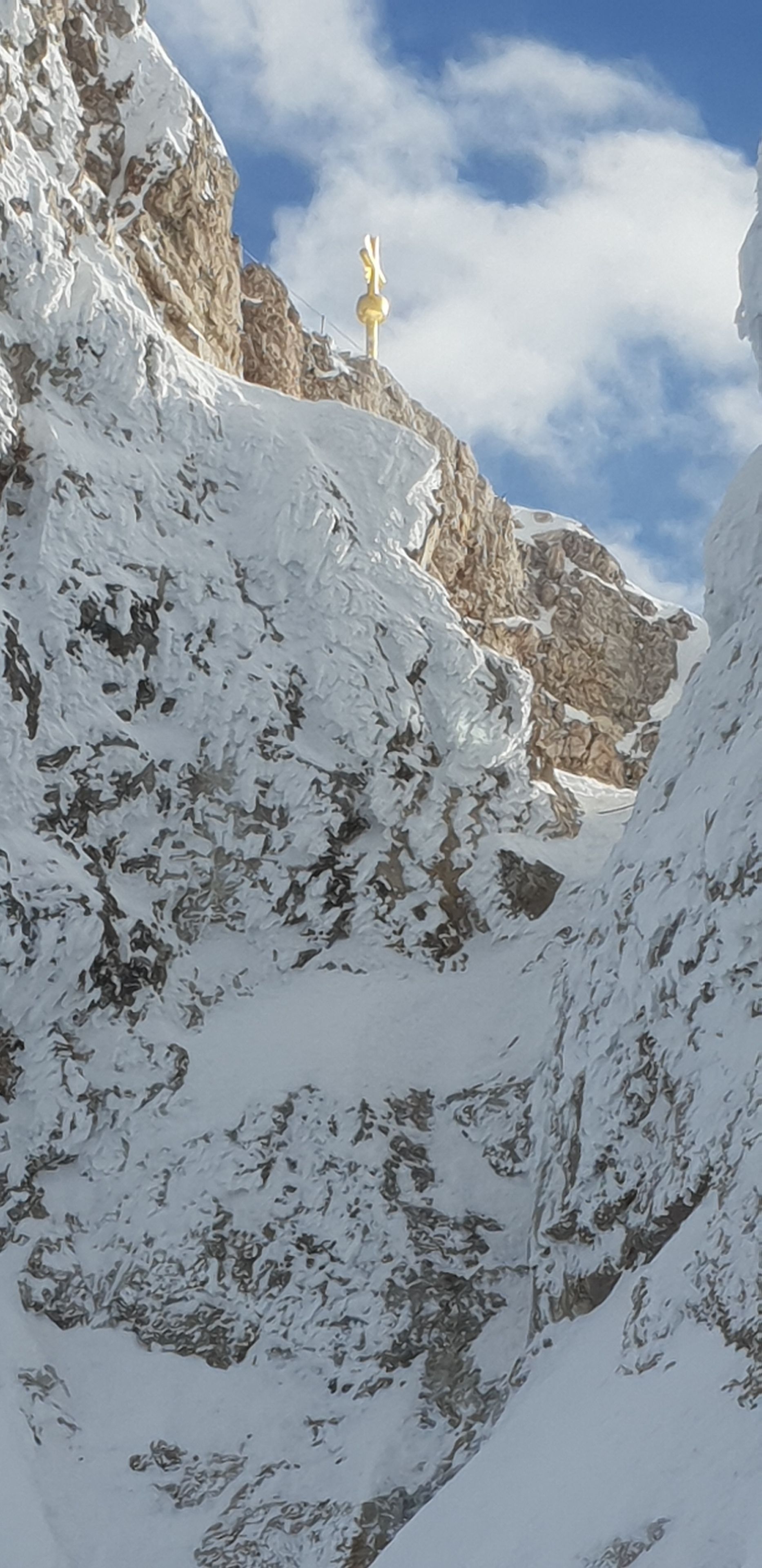 Una montaña nevada con una estatua dorada en una cima rocosa.