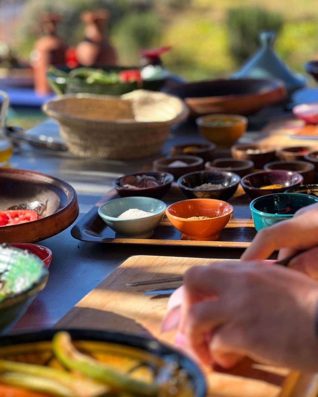 A table with various bowls containing food items, a person’s hand, and a knife on a wooden board.