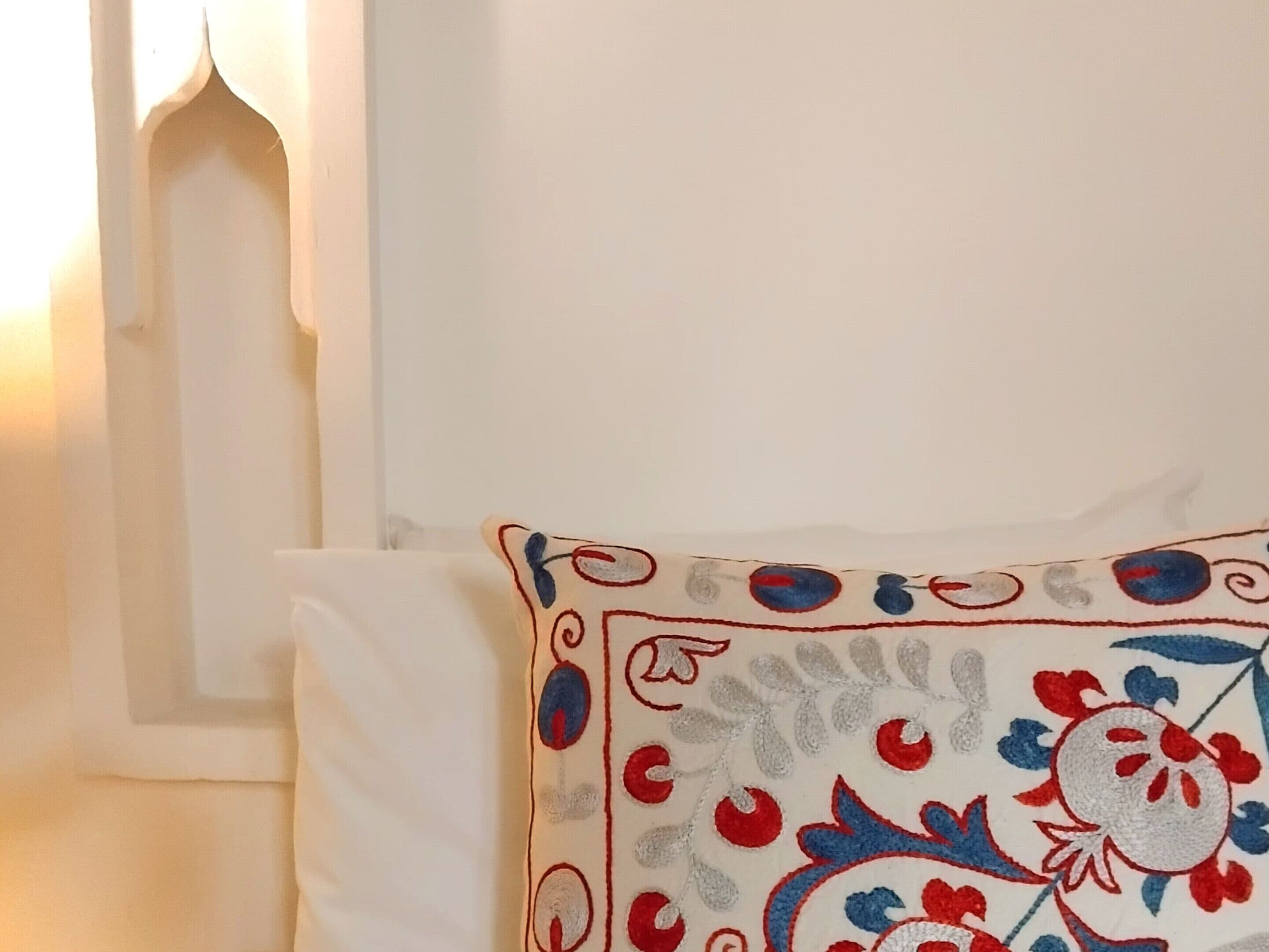 A white pillow with a red, blue, and gray embroidered floral pattern.