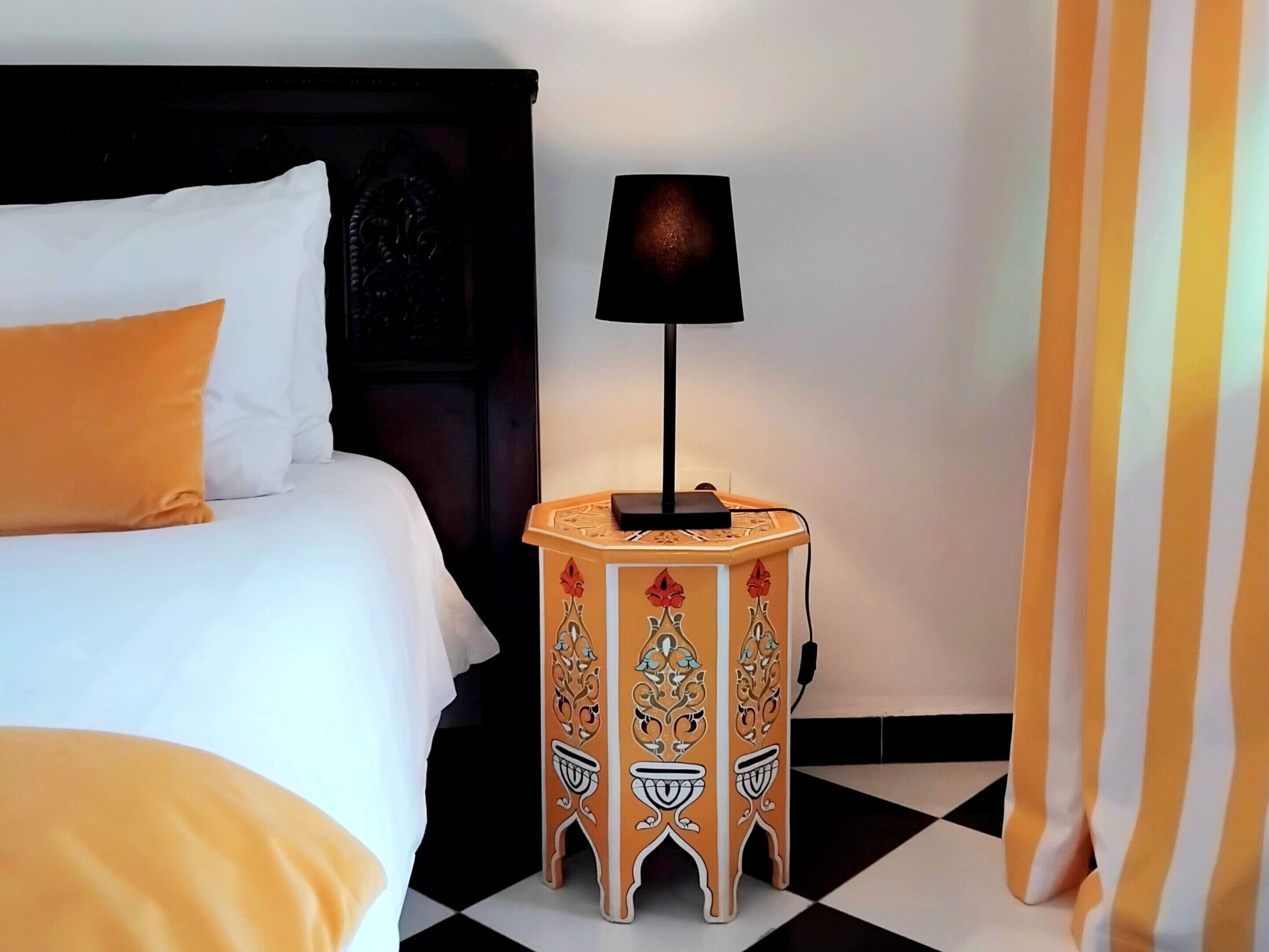 A hotel room with a bed, a nightstand with a lamp, and a checkered floor.