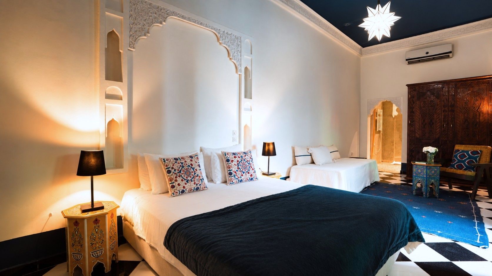 Una camera d'albergo con un letto grande, due comodini, un tavolino da notte, un pannello decorativo e un tappeto a motivi.