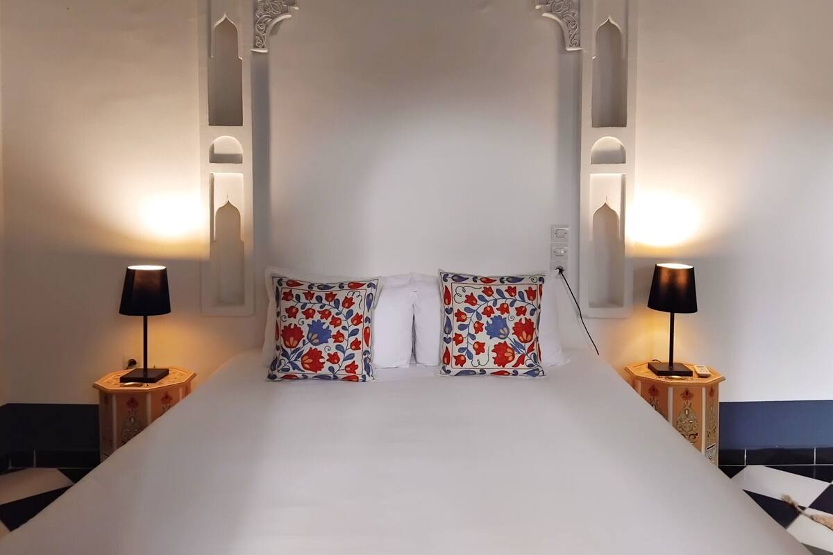 A bed with white linens, two pillows with floral patterns, and two bedside lamps on matching nightstands.