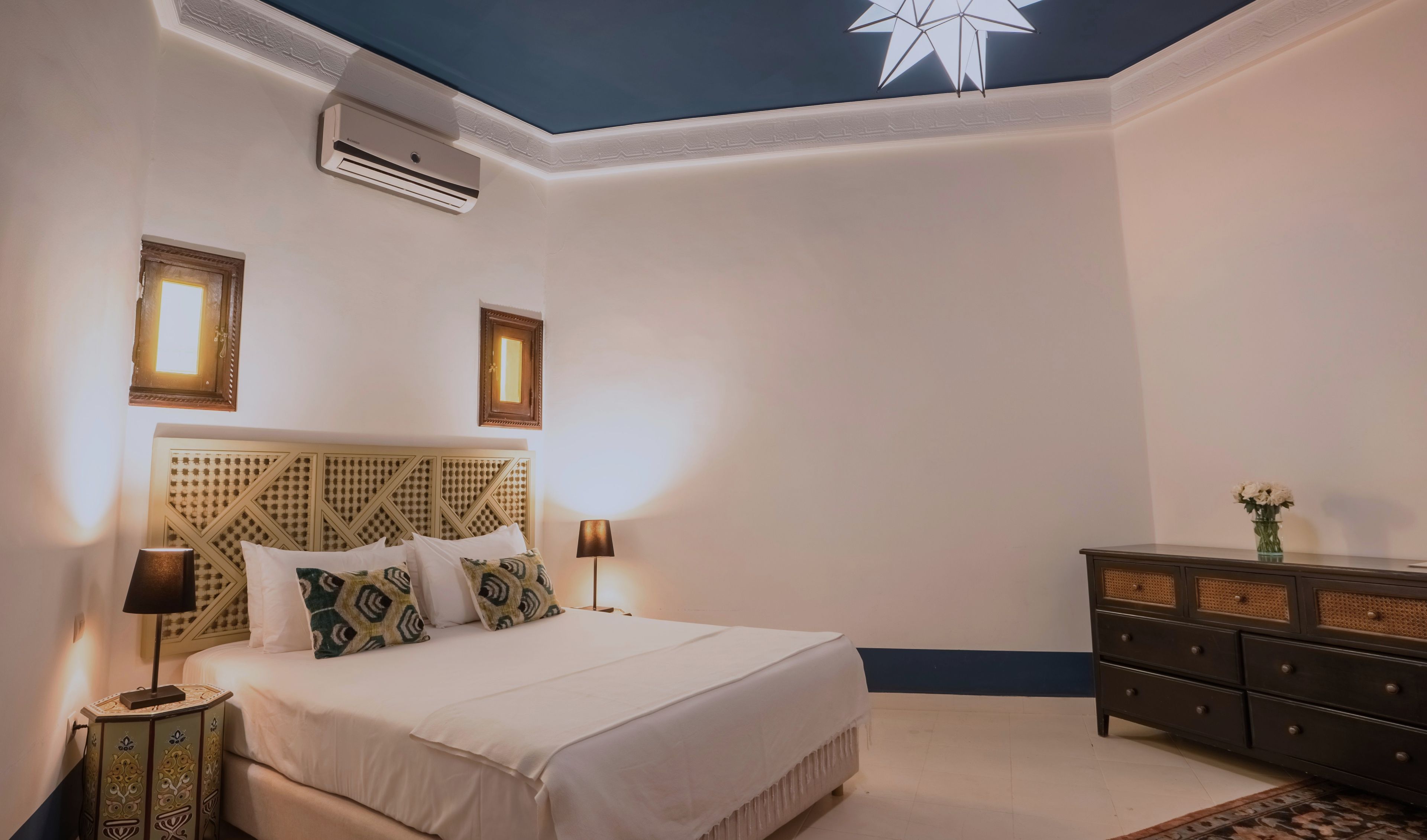 Een slaapkamer met een bed, nachtlampjes, een dressoir en een airconditioning.