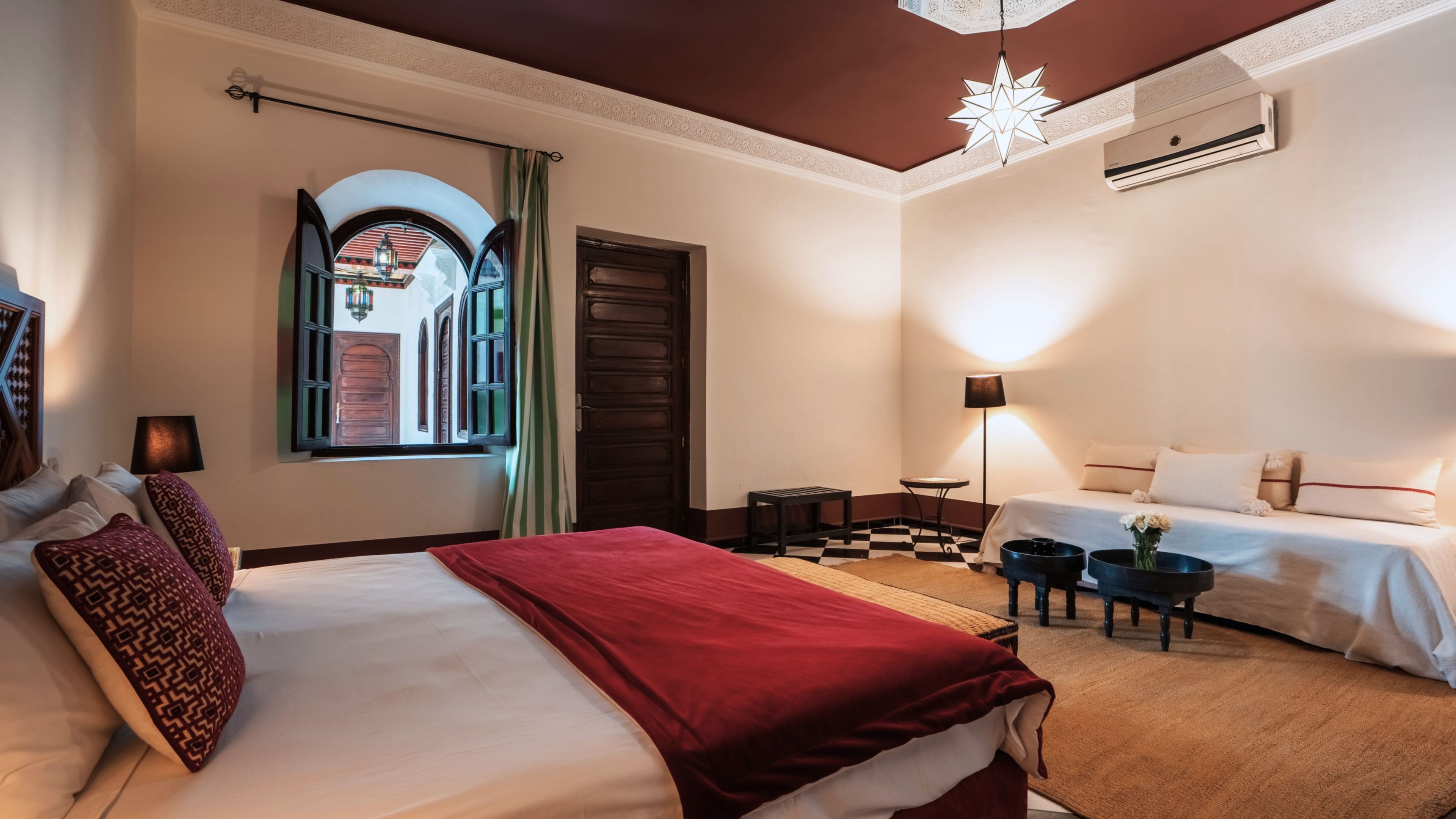 A hotel room with a large bed, a smaller bed, a desk, a chair, a lamp, and a decorative ceiling light.