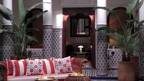 Un interior tradicional marroquí con un sofá, plantas en macetas y azulejos estampados.