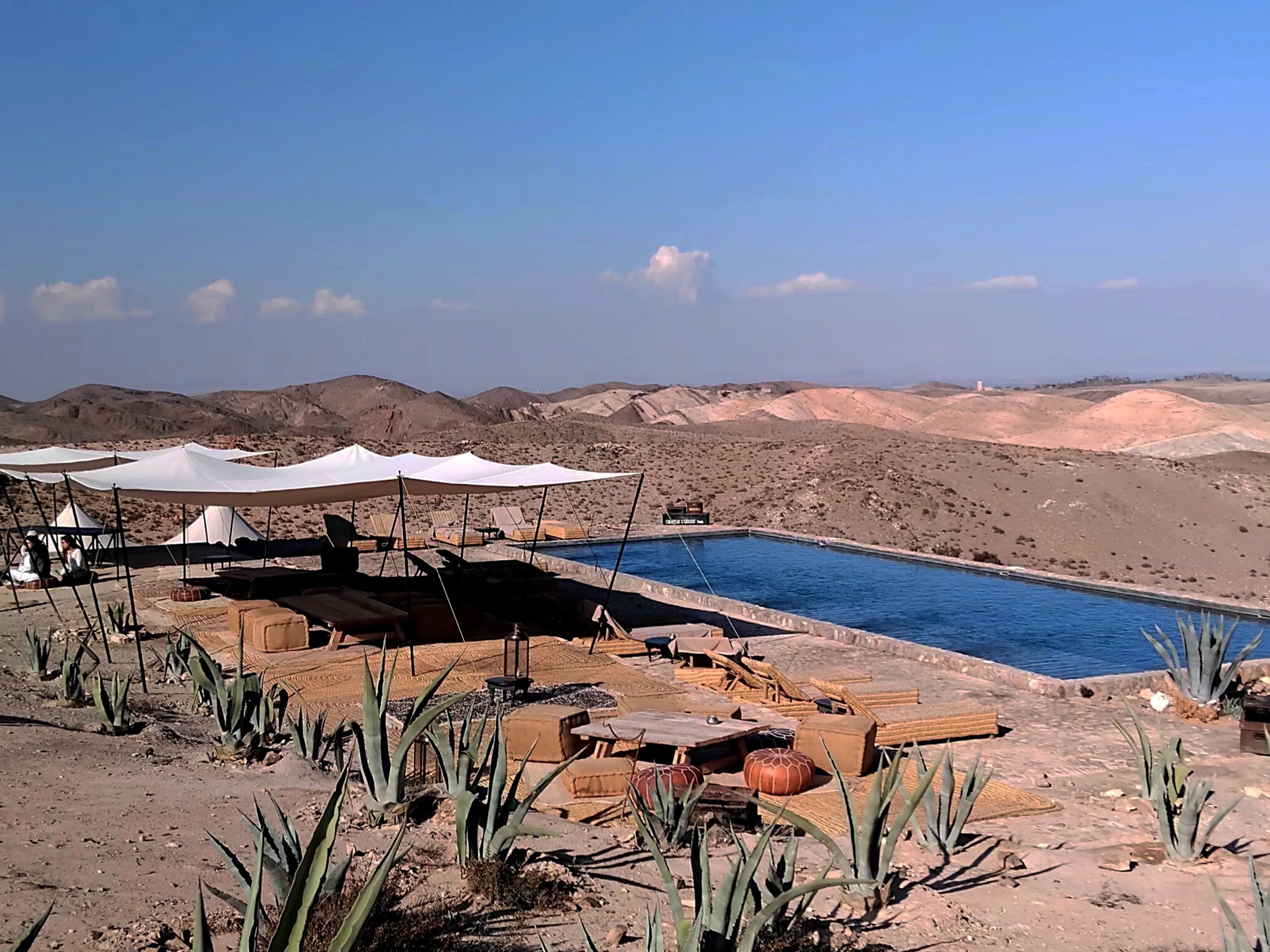 Un paysage désertique avec une piscine, des tentes blanches et des chaises longues.