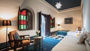 Ein Hotelzimmer mit einem Bett, einem Sessel, einem kleinen Tisch mit einer Vase, einem gemusterten Teppich und einer dekorativen Deckenleuchte.