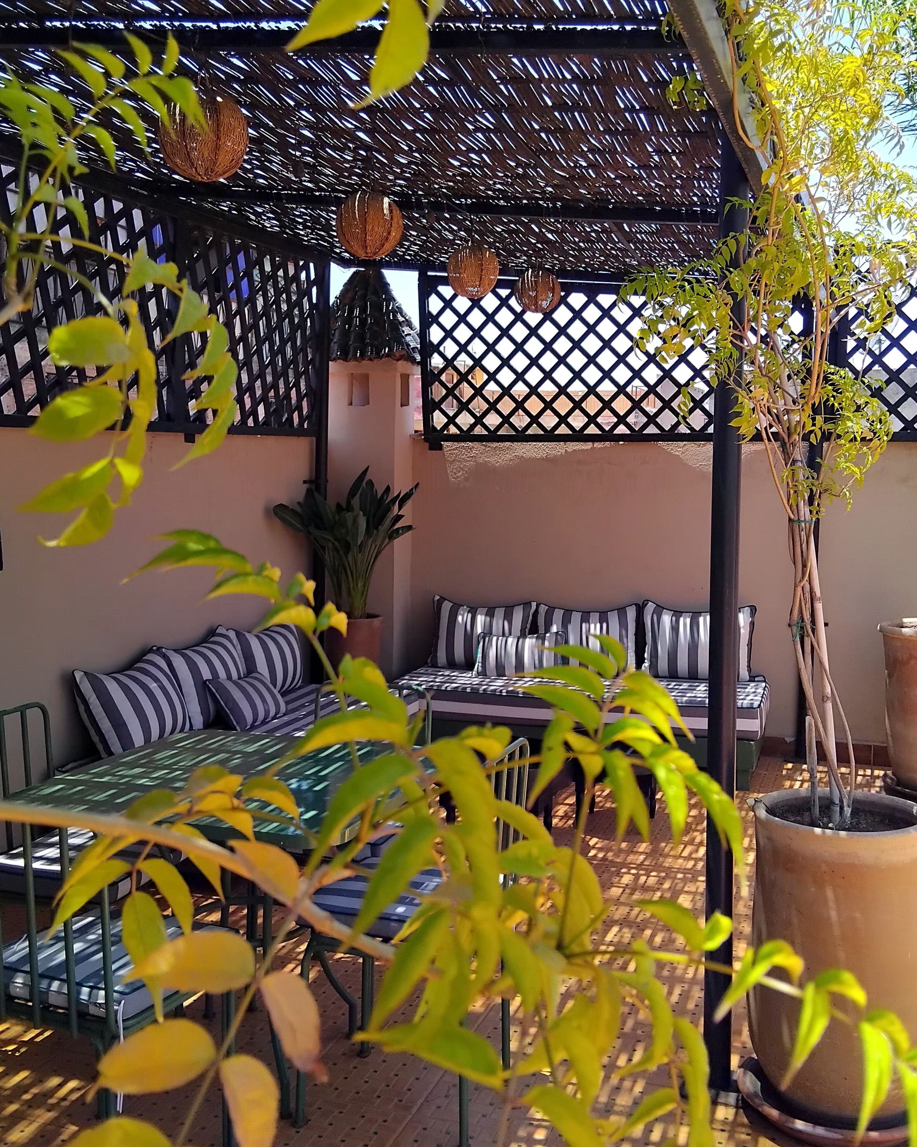 Un área de estar al aire libre techada con cojines a rayas, techo tejido y plantas en macetas.
