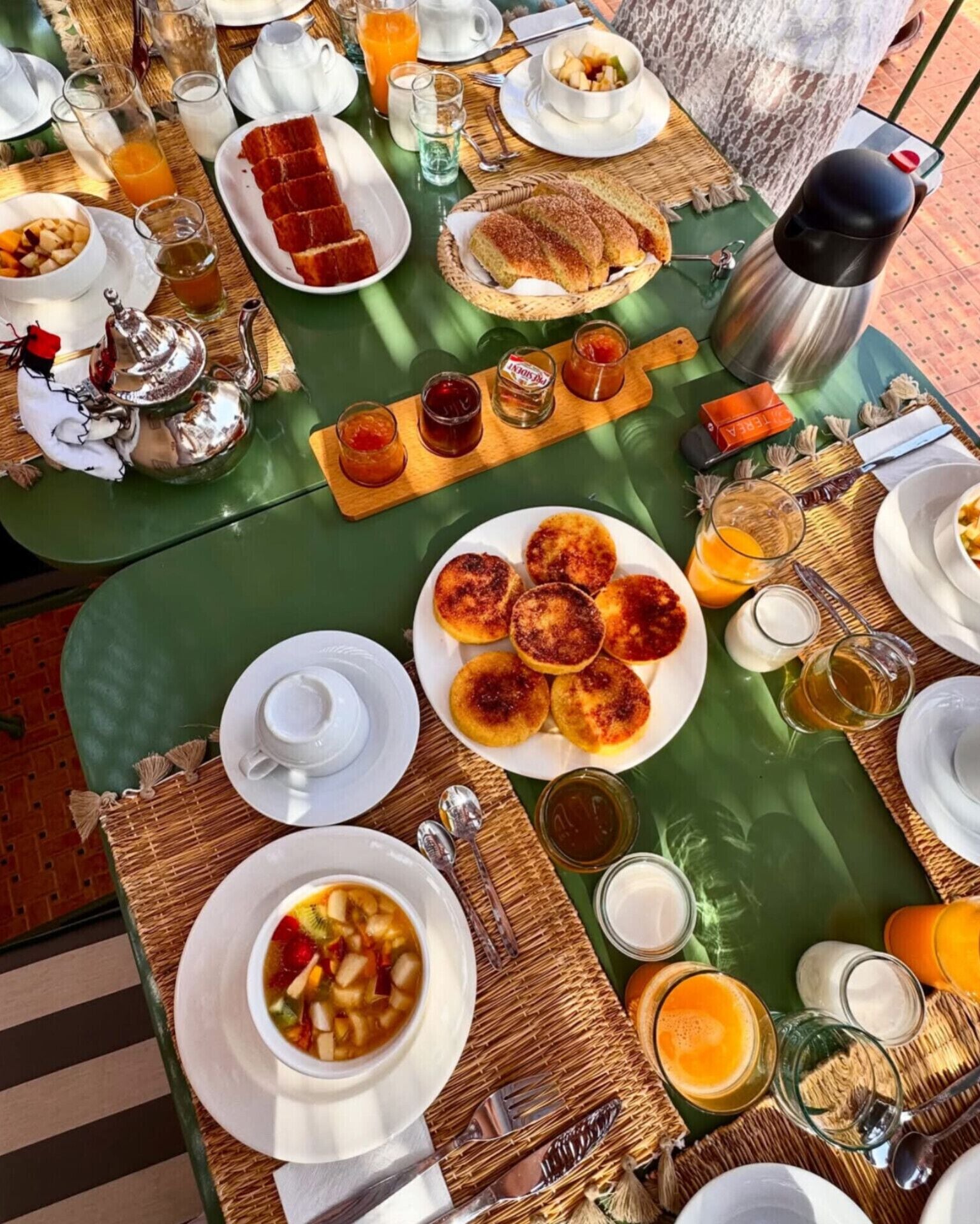 Ein Frühstückstisch mit verschiedenen Speisen, darunter Pfannkuchen, Obst und ein heißes Getränk.