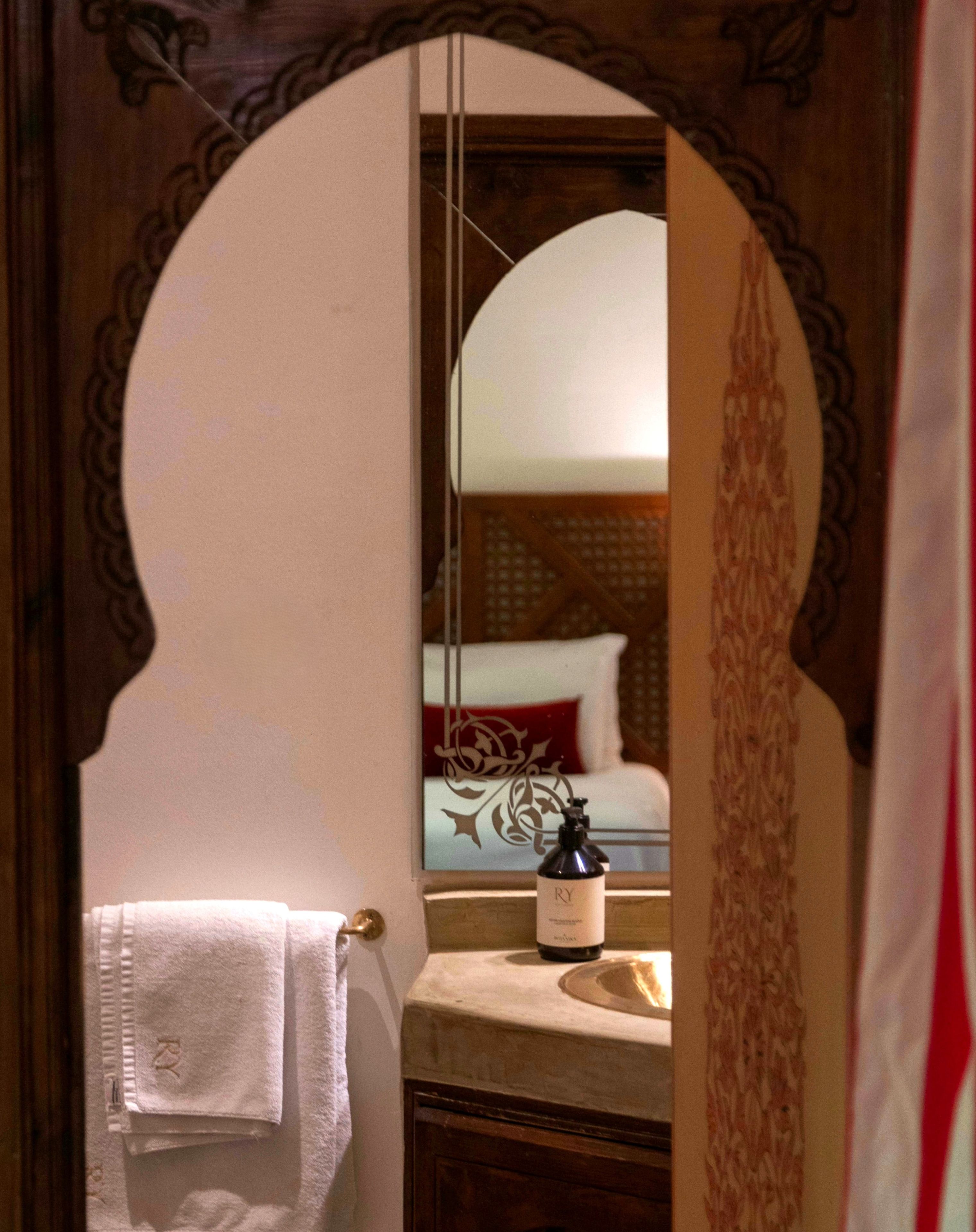 A bathroom with a mirror, a towel hanging on a rack, and a bottle on the sink.