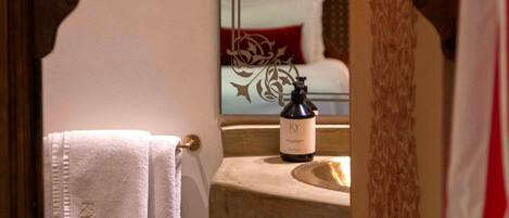 A bathroom with a mirror, a towel hanging on a rack, and a bottle on the sink.