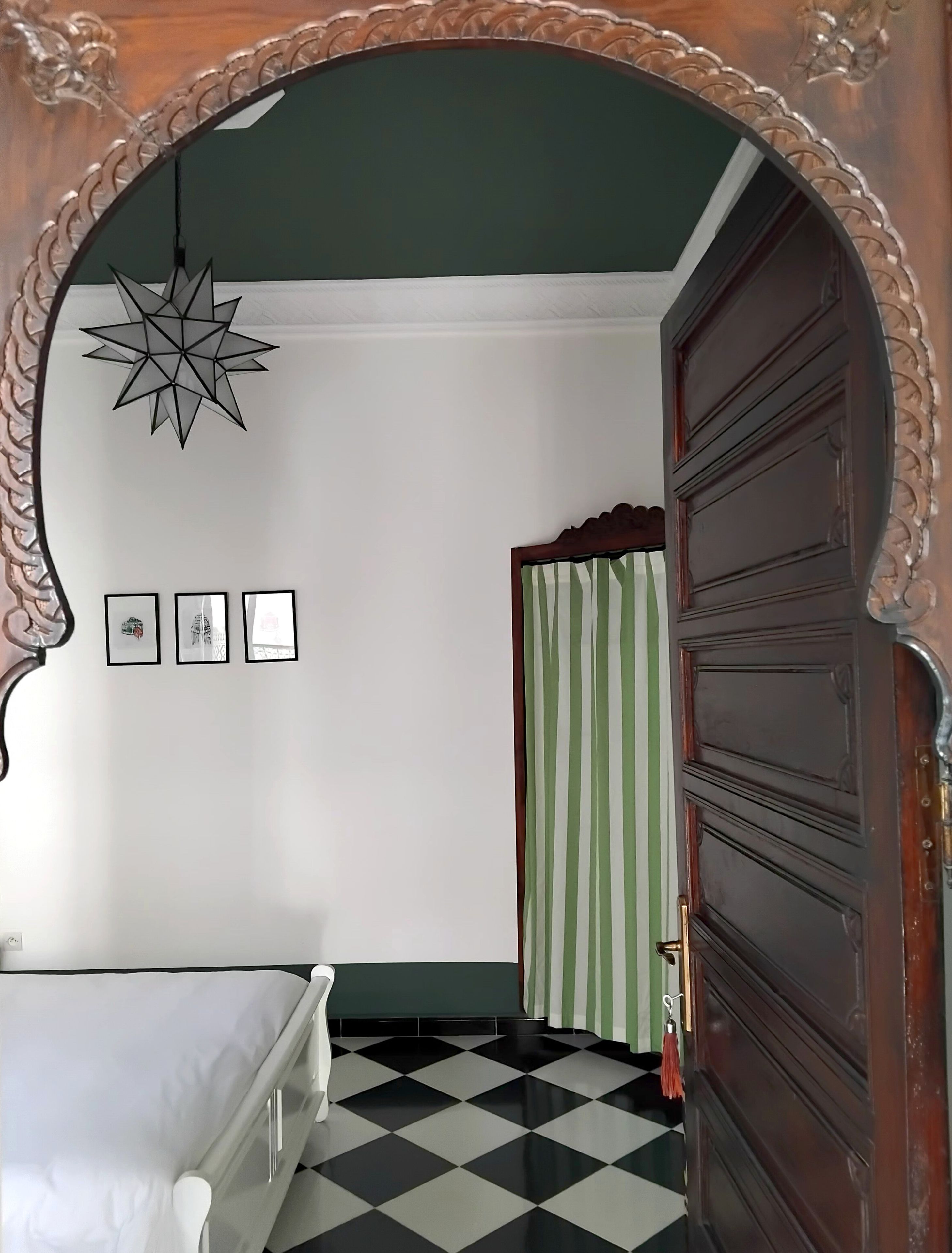 Een kamer met een zwart-wit geruit vloerkleed, een bed, een ster-vormige hanglamp en een deur met een gestreept gordijn.