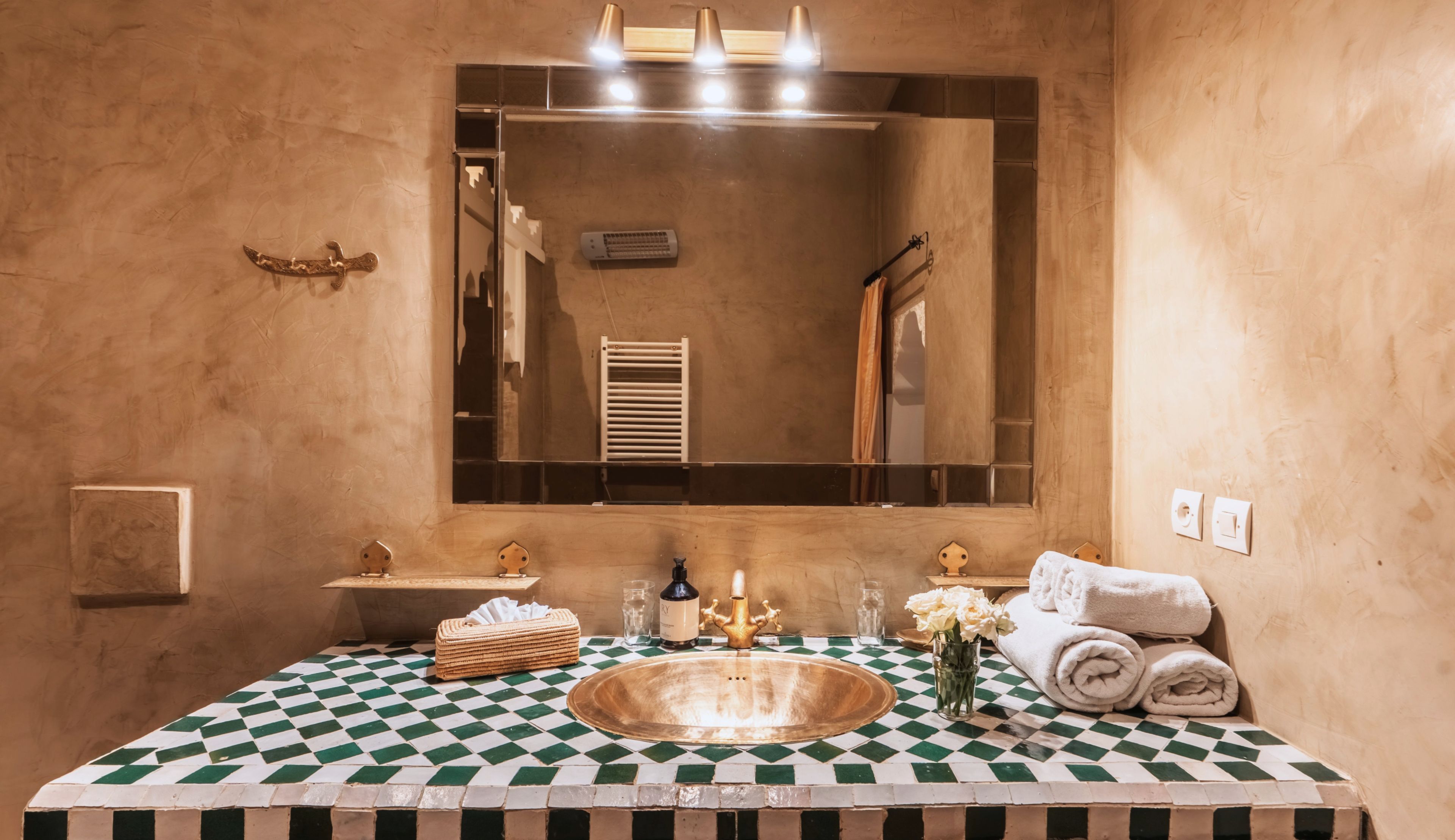 Un bagno con pavimento a scacchi, uno specchio grande, un lavandino e degli asciugamani.