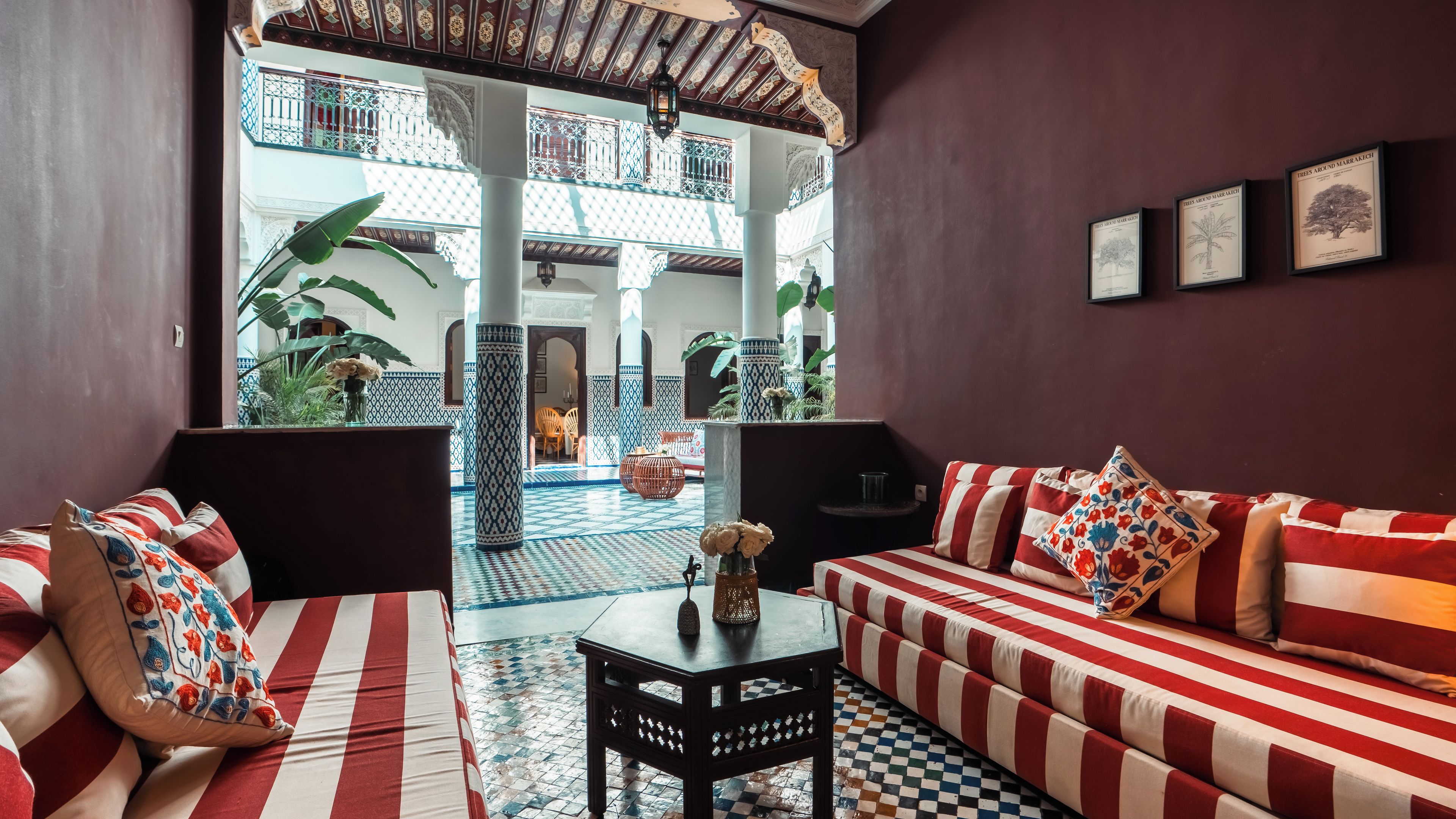A hotel lobby with a checkered floor, a sofa set, a small table with a vase, and a view of the courtyard.