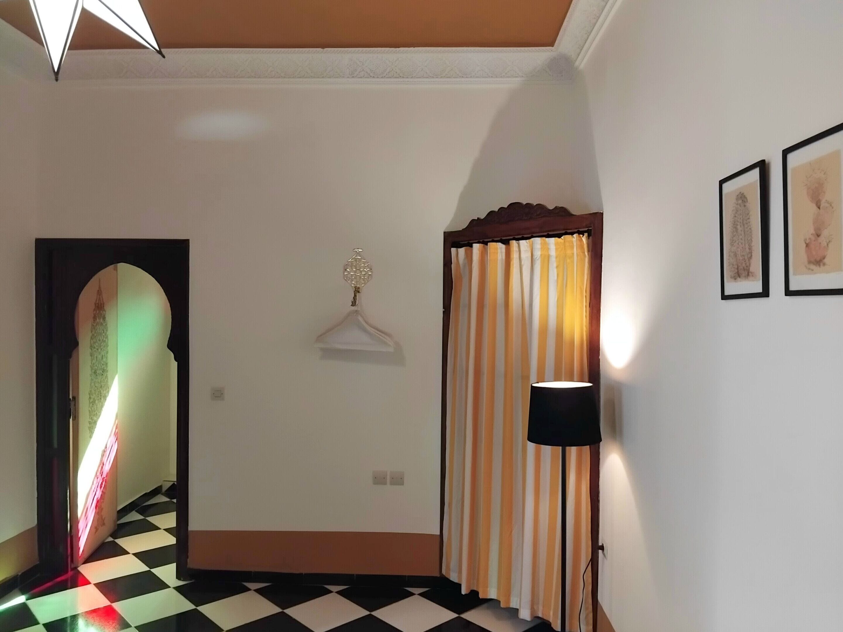 Un pasillo con piso a cuadros, un candelabro colgante, una cortina a rayas y obras de arte enmarcadas en la pared.