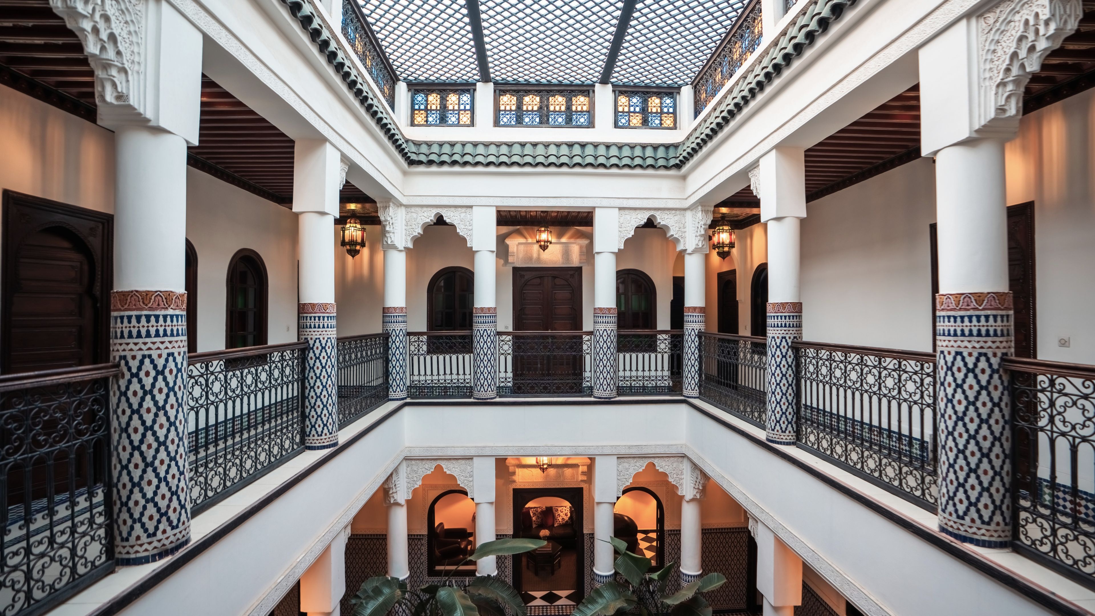 Un intérieur à plusieurs niveaux, agrémenté de colonnes décoratives, d’un escalier central et d’un balcon offrant une vue sur le niveau inférieur.