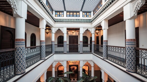 Interior de varios niveles con columnas ornamentales, una escalera central y un balcón con vista al nivel inferior.