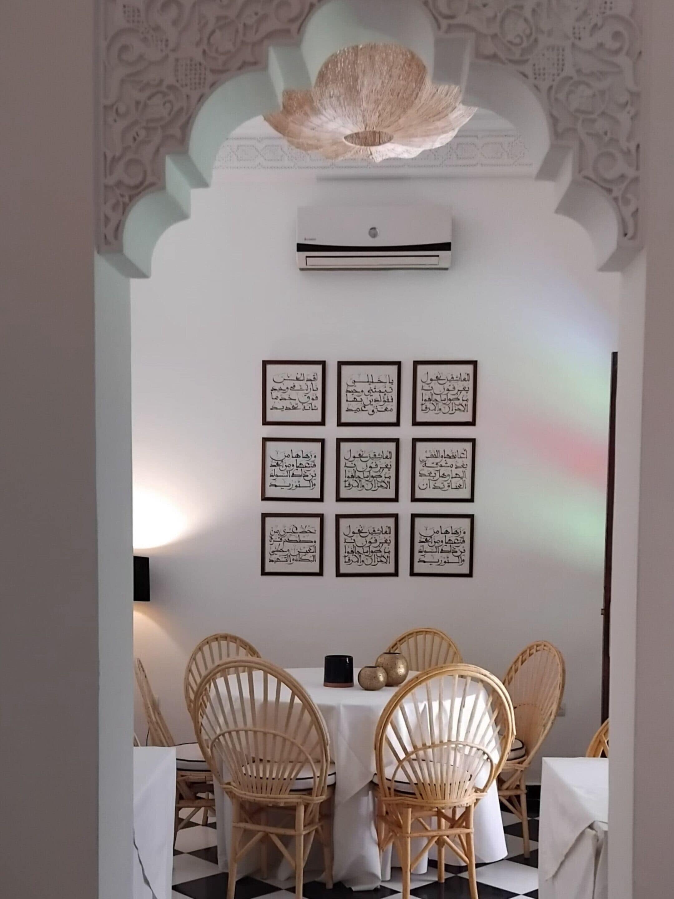 Ein Essbereich mit einem weißen Tisch und Stühlen, an der Wand Kalligrafie-Kunst und eine kunstvolle Deckenleuchte.