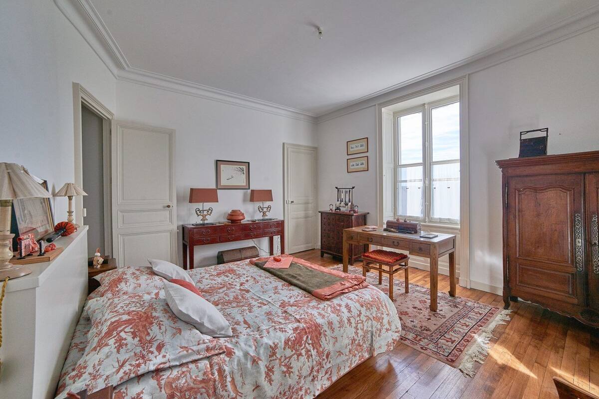 Een slaapkamer met een bed, een bureau, een dressoir en een raam.