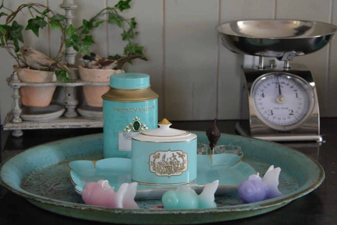 Un plan de travail de cuisine agrémenté d’une balance de couleur turquoise, d’un bocal turquoise orné de motifs dorés et d’une assiette décorative turquoise sur laquelle est posée une figurine d’oiseau.