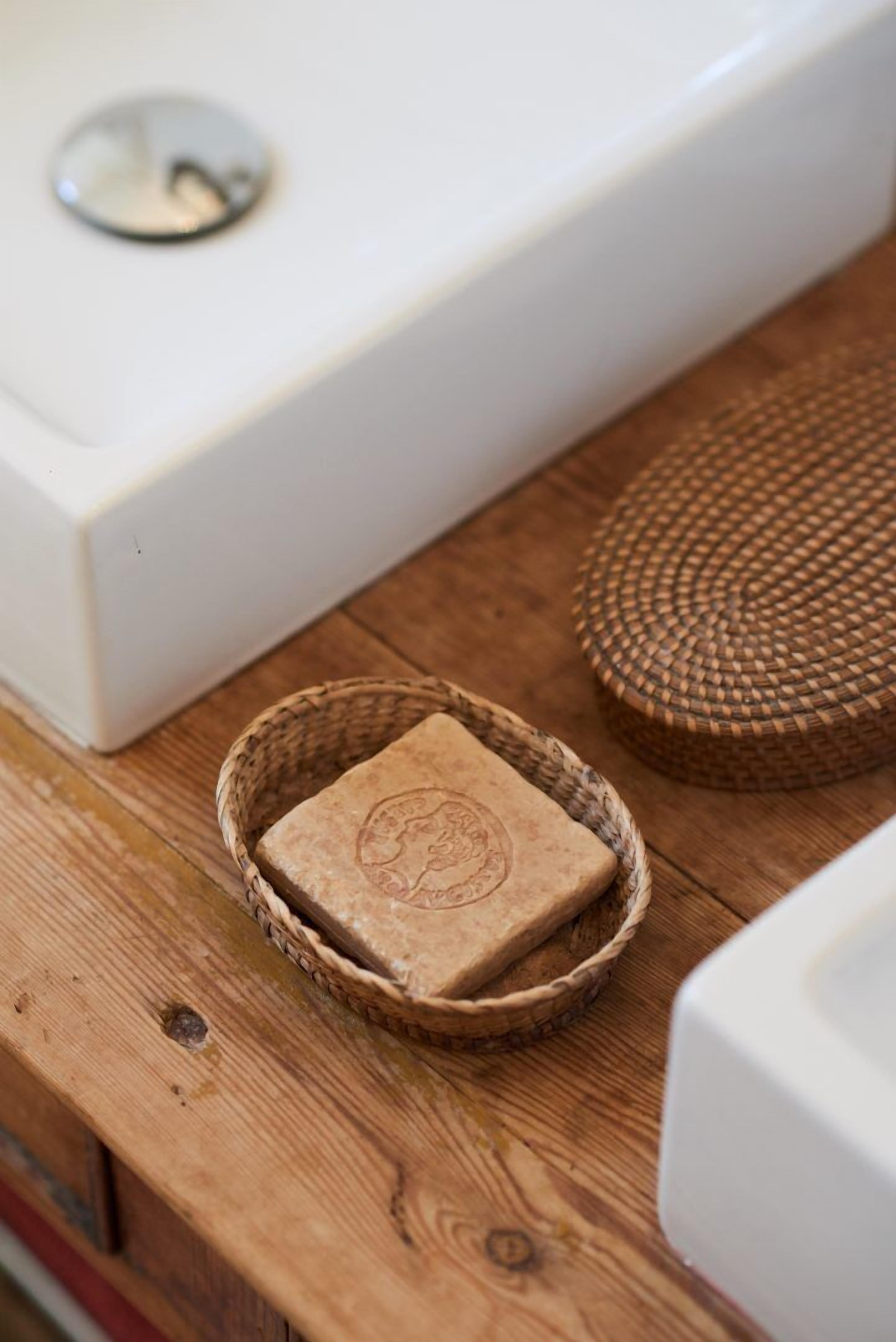 A wooden table with a woven basket containing a soap bar, a woven mat, and a white appliance.
