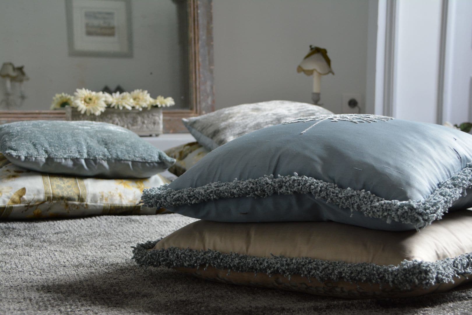 Ein Schlafzimmer mit einem Bett, das mit vielen Kissen bezogen ist, einem Spiegel und einer Vase mit Blumen.