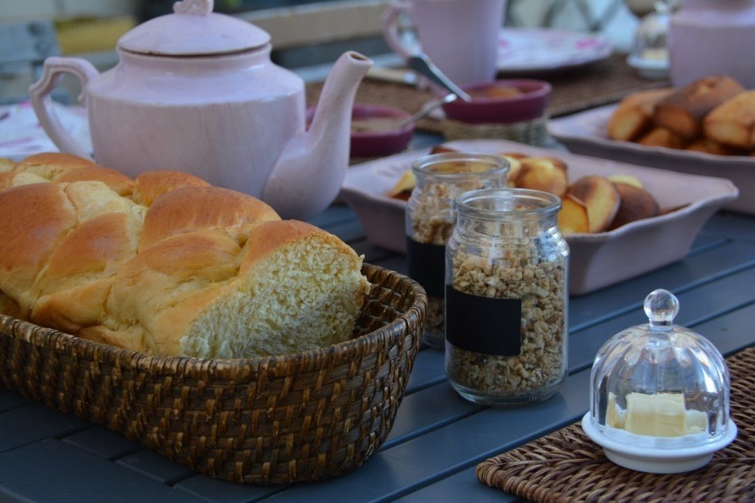 Una mesa con una cesta de pan, un calentador de té, botes de mermelada y un cuencos de mantequilla.