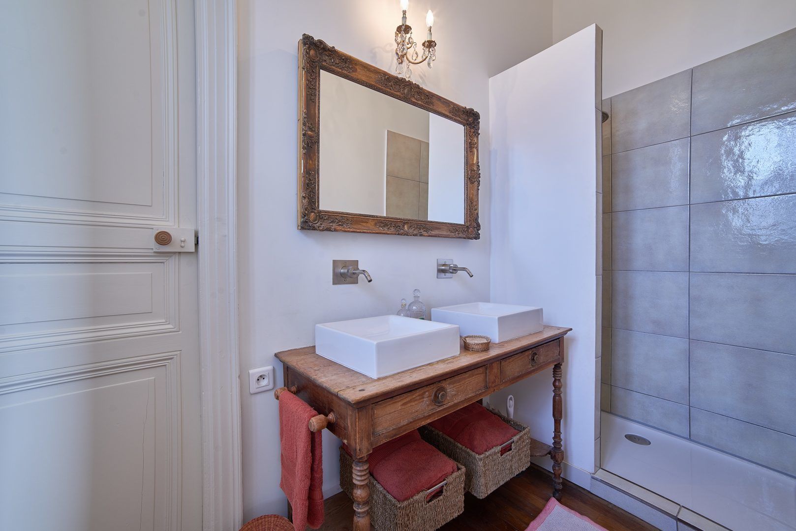 Une salle de bain avec deux lavabos, un miroir, un meuble-lavabo en bois et un espace douche.