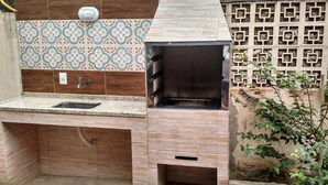 An outdoor kitchen with a built-in grill, a sink, and a tiled backsplash.