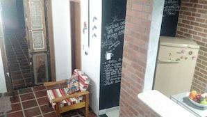 A kitchen with a refrigerator, a chair, and a blackboard with writing.