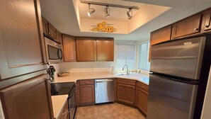 Una cocina compacta con armarios de madera, un refrigerador de acero inoxidable, lavavajillas y microondas.