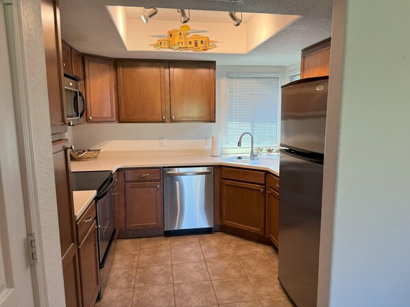 A compact kitchen with wooden cabinets, a stainless steel dishwasher, and a refrigerator.
