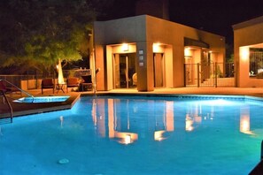 Une piscine avec un bâtiment moderne en arrière-plan, un espace de repos couvert et une entrée fermée par un portail.