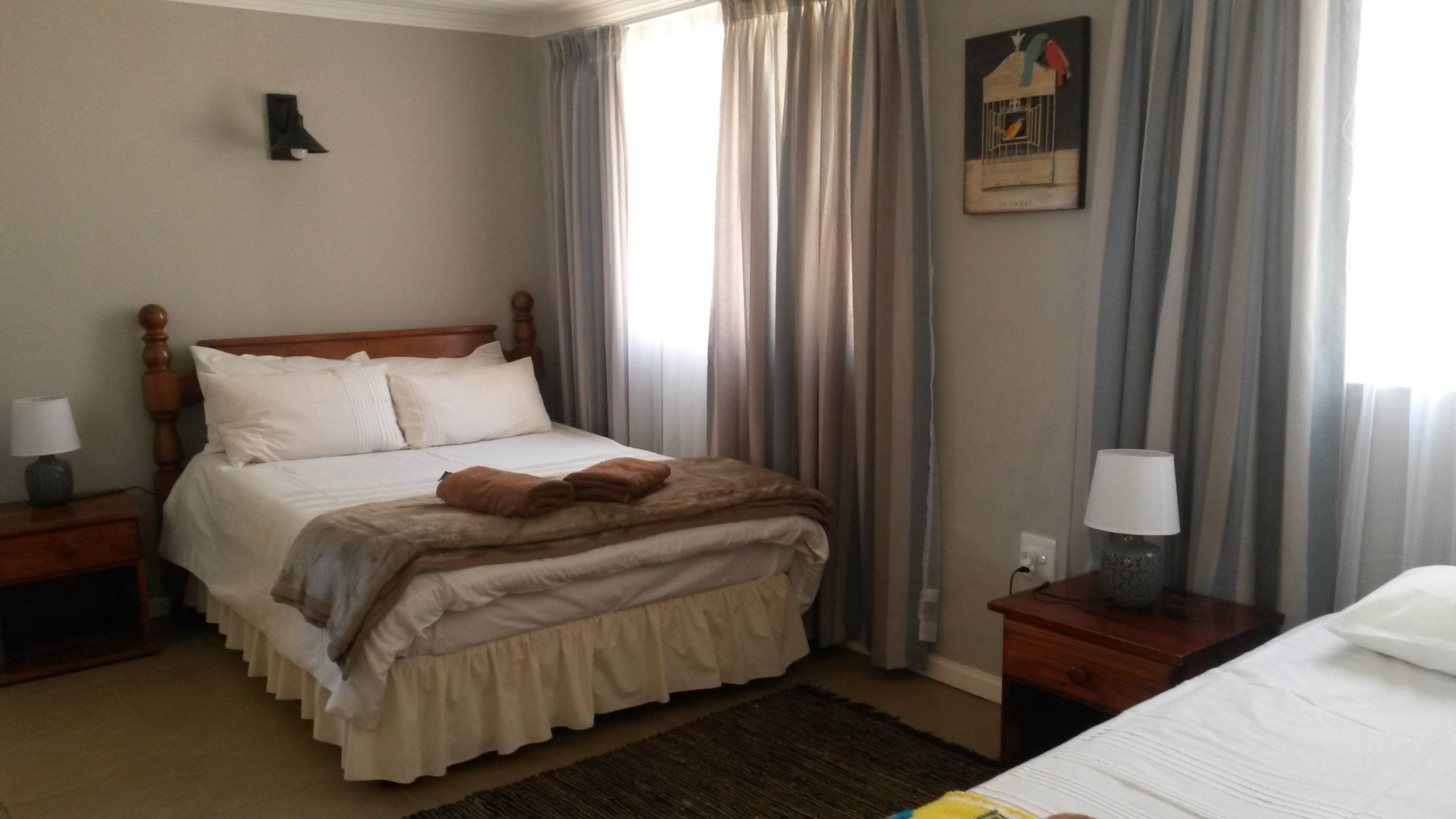 A neatly made bed with a brown throw blanket and pillows, a wooden headboard, a bedside lamp, and a framed picture on the wall.