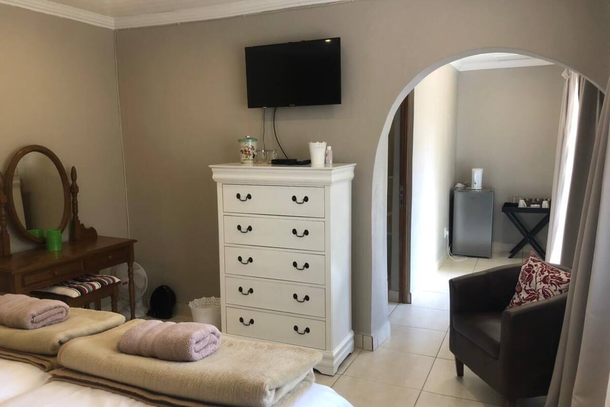 Une chambre d’hôtel avec un lit, une commode blanche, une télévision, un miroir et une chaise.