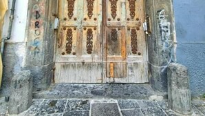 A large, ornate wooden door with intricate carvings, set within an arched doorway, flanked by stone pillars and a stone-paved entrance. - Andrea's House Apartment in the Historic Center of Naples (Naples)