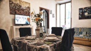 A dining area with a table set for four, a vase with flowers, and a television on the wall. - Andrea's House Apartment in the Historic Center of Naples (Naples)