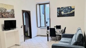 A living room with a sofa, a TV, a dining table with chairs, and artwork on the walls. - Andrea's House Apartment in the Historic Center of Naples (Naples)
