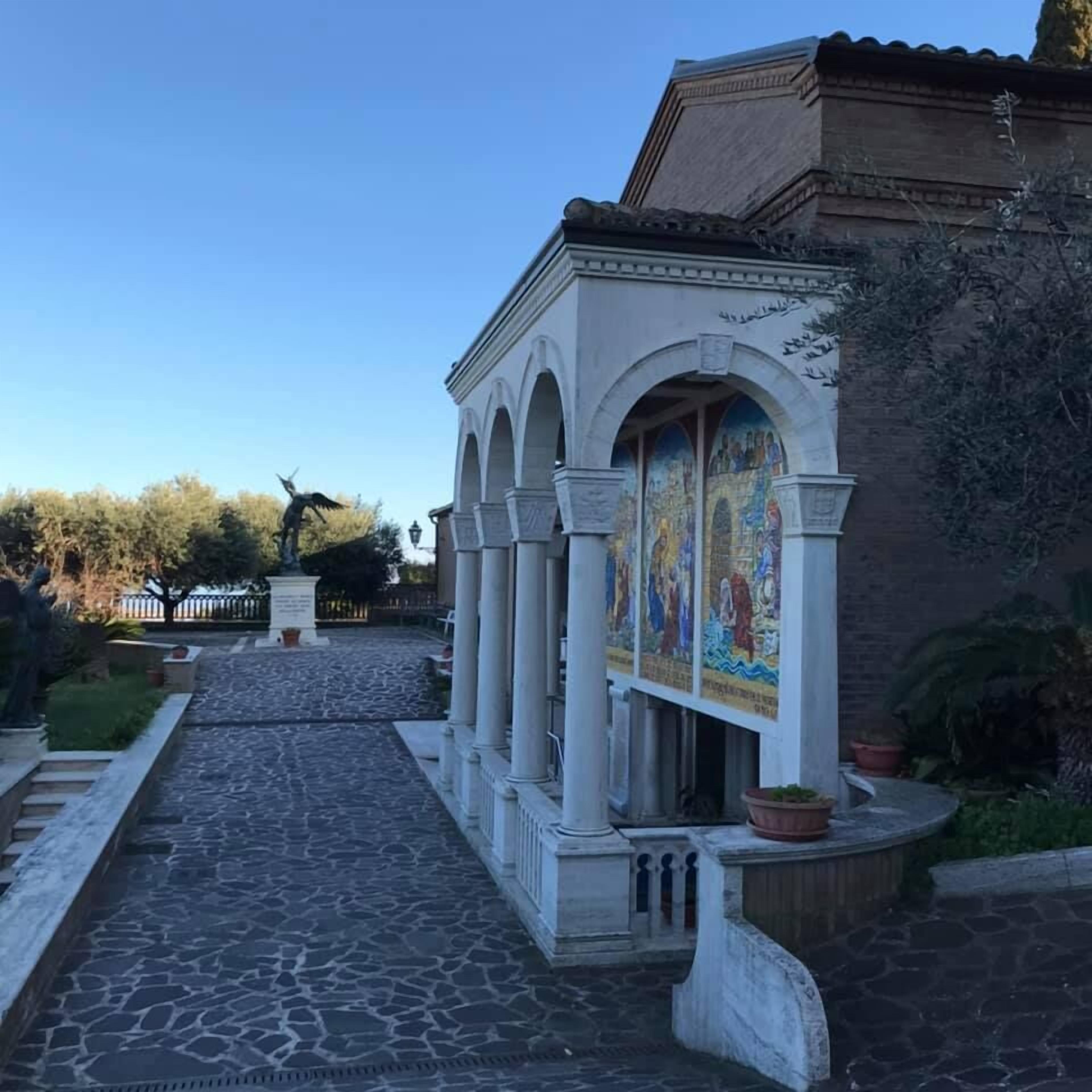 Un chemin de pierre mène à un bâtiment doté d’une entrée en arc de cercle et orné d’une fresque murale.