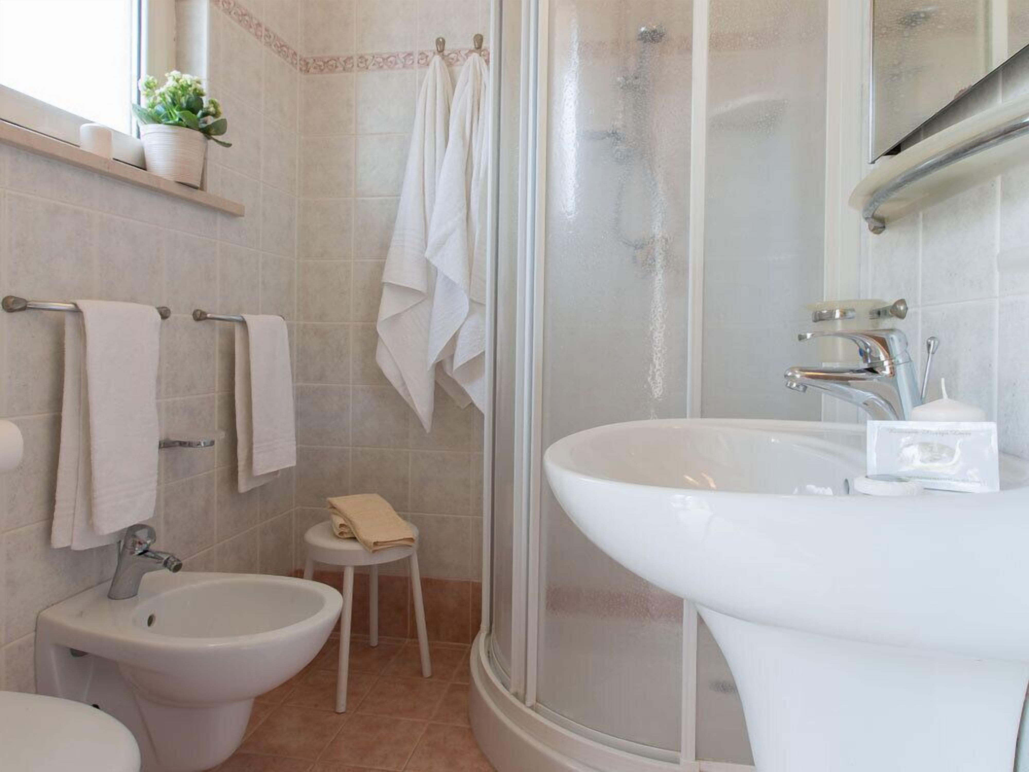 A bathroom with a bidet, a sink, a shower, and a small stool.