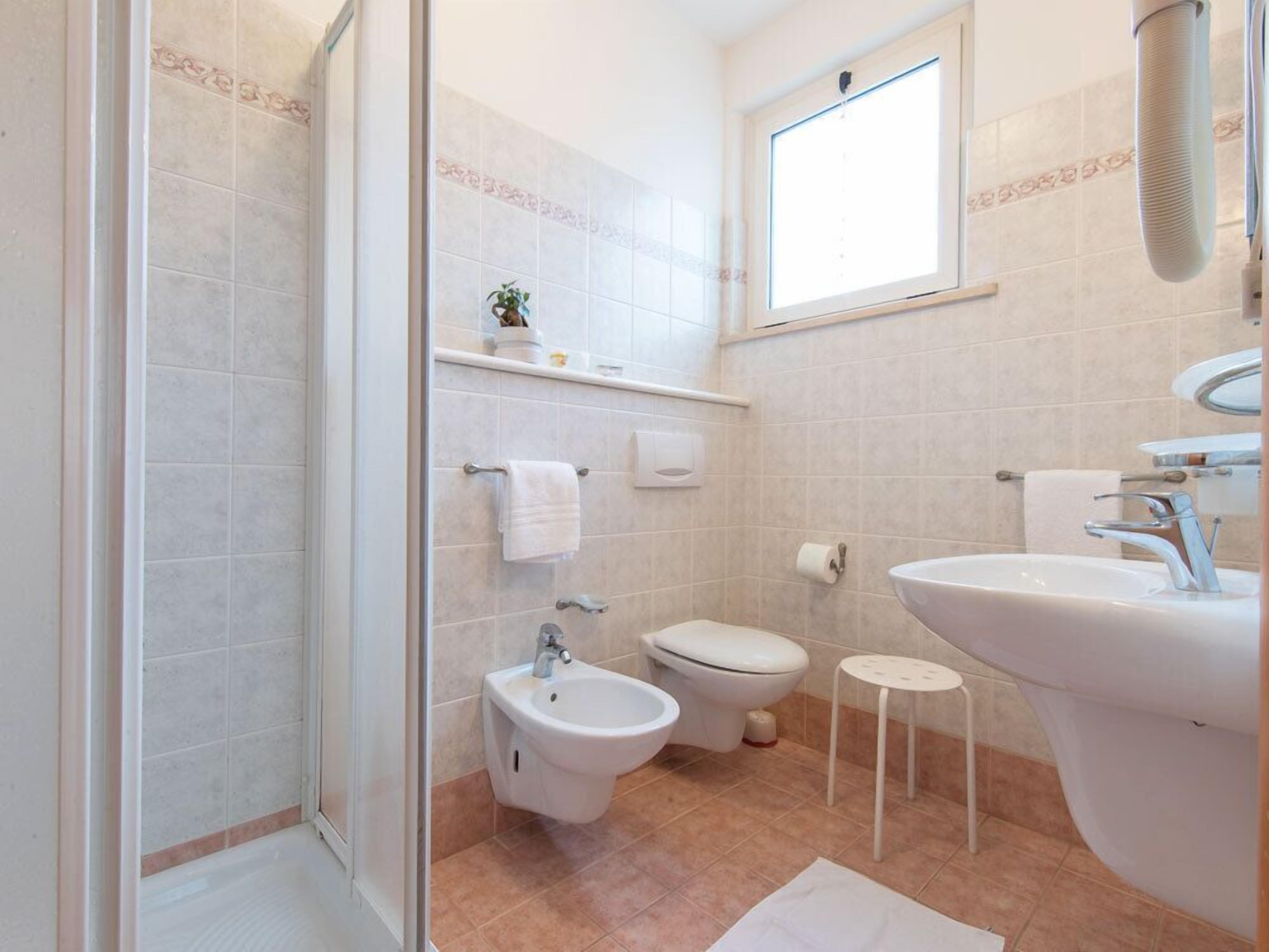 Un baño con ducha, bidé, inodoro, lavamanos y un taburete pequeño.