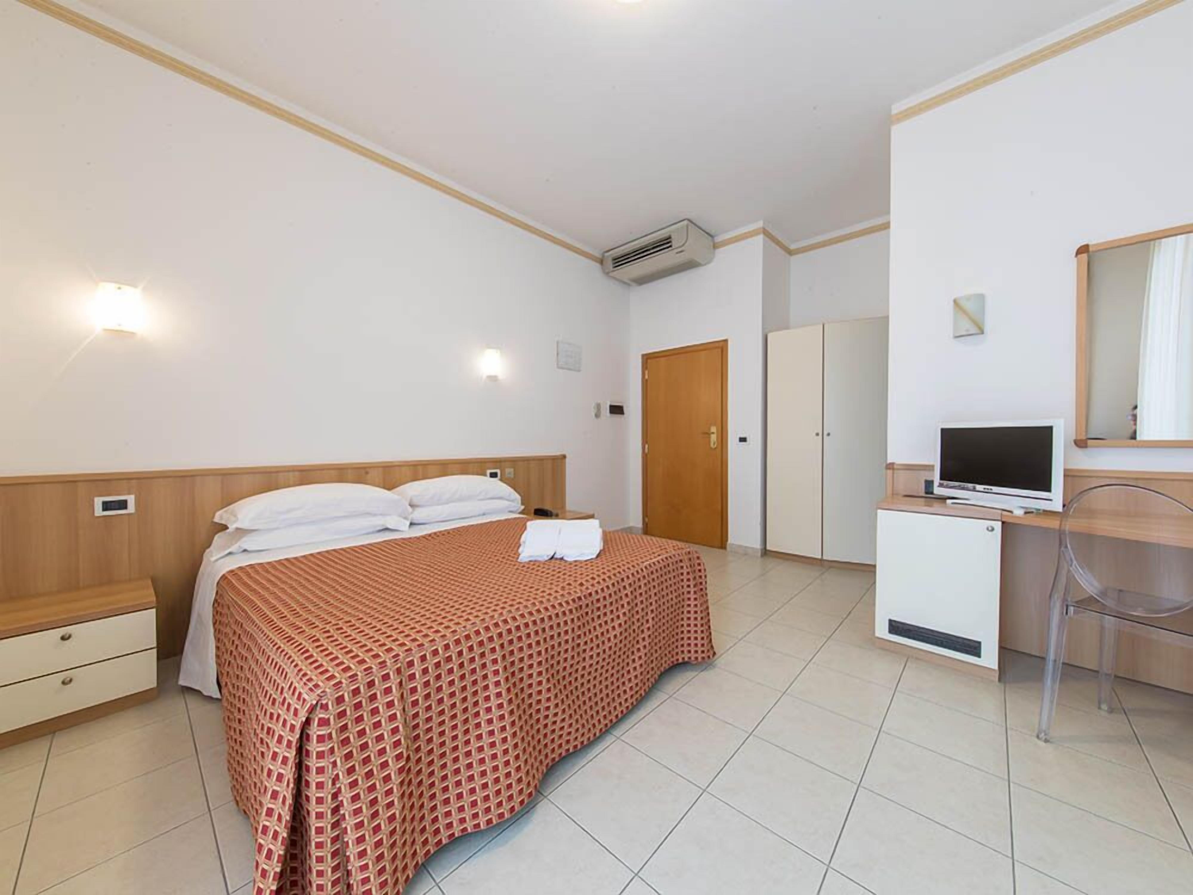 Una habitación de hotel con cama, escritorio con computadora, armario y puerta.
