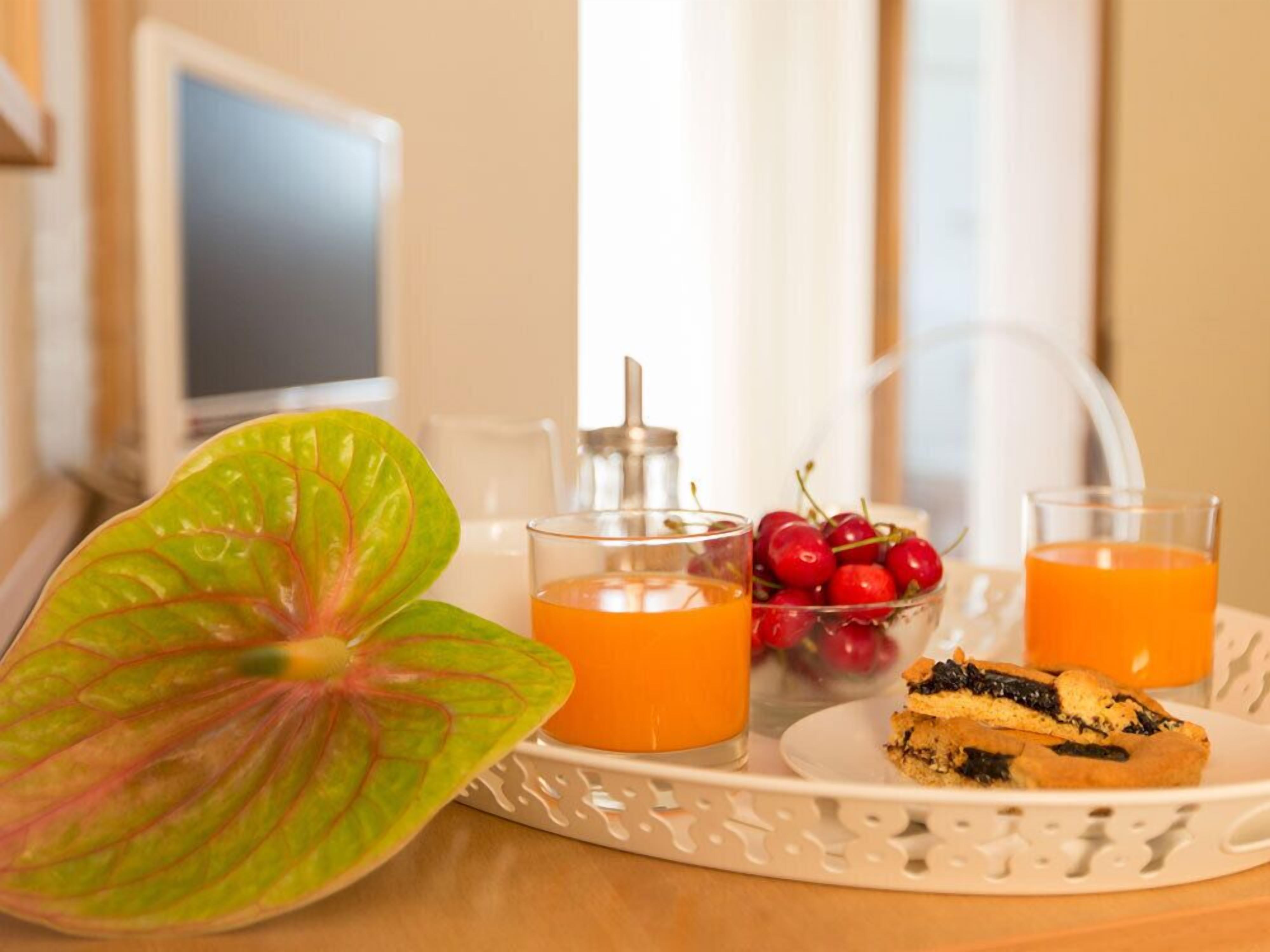 Bandeja de café da manhã com suco de laranja, três copos de suco de laranja e um prato com muffin, além de uma tigela de cerejas.