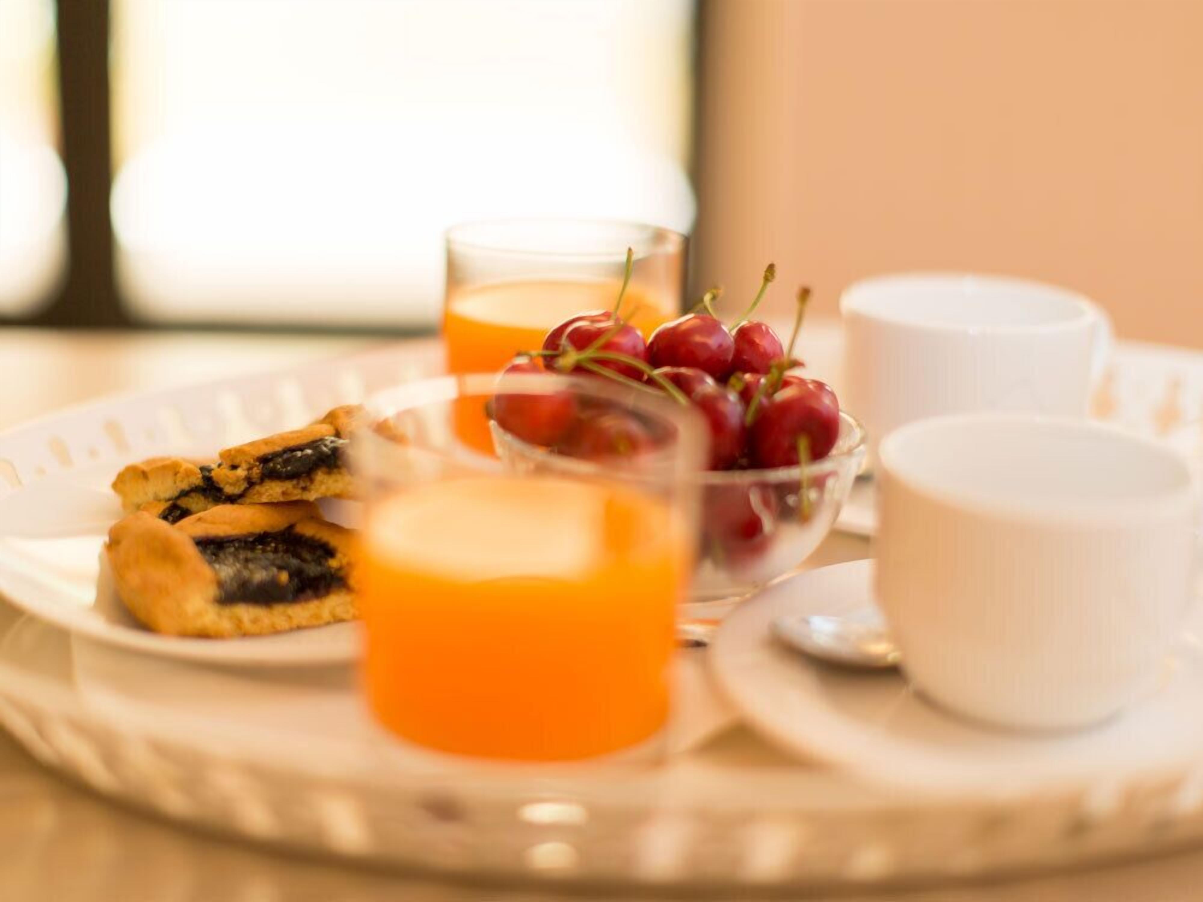 A breakfast tray with pastries, a bowl of cherries, and two glasses of orange juice.
