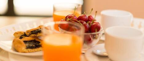 A breakfast tray with pastries, a bowl of cherries, and two glasses of orange juice.